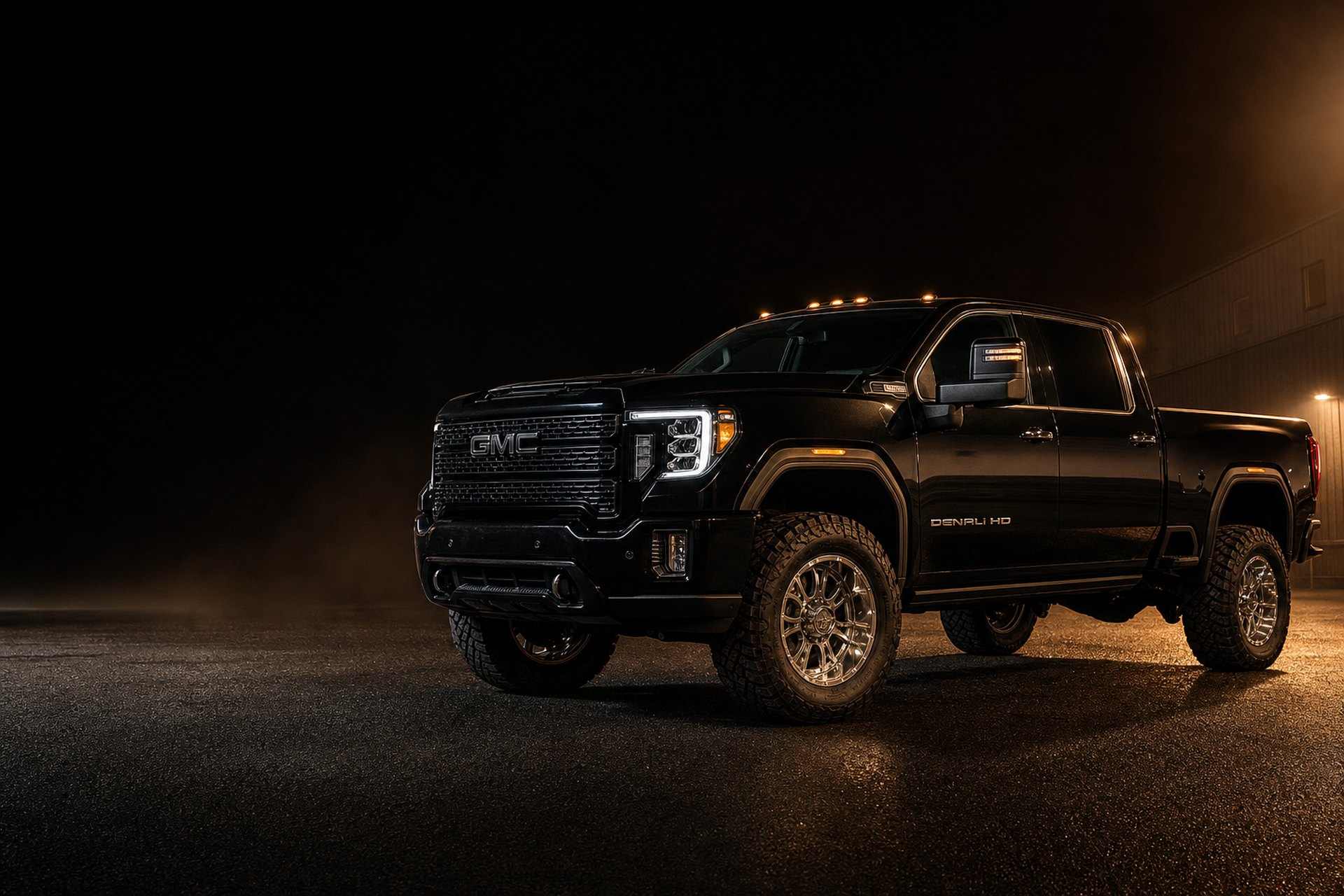 Black lifted GMC Sierra Denali HD pickup on aggressive tires at night